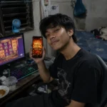 ภาพผู้เล่นถือโทรศัพท์แสดง Mega Win พร้อมเกมสล็อตบนหน้าจอคอมพิวเตอร์ ใช้ประกอบเนื้อหาแนะนำเกมสล็อต TB68 และวิธีเล่นสล็อตสำหรับผู้เริ่มต้นปี 2026